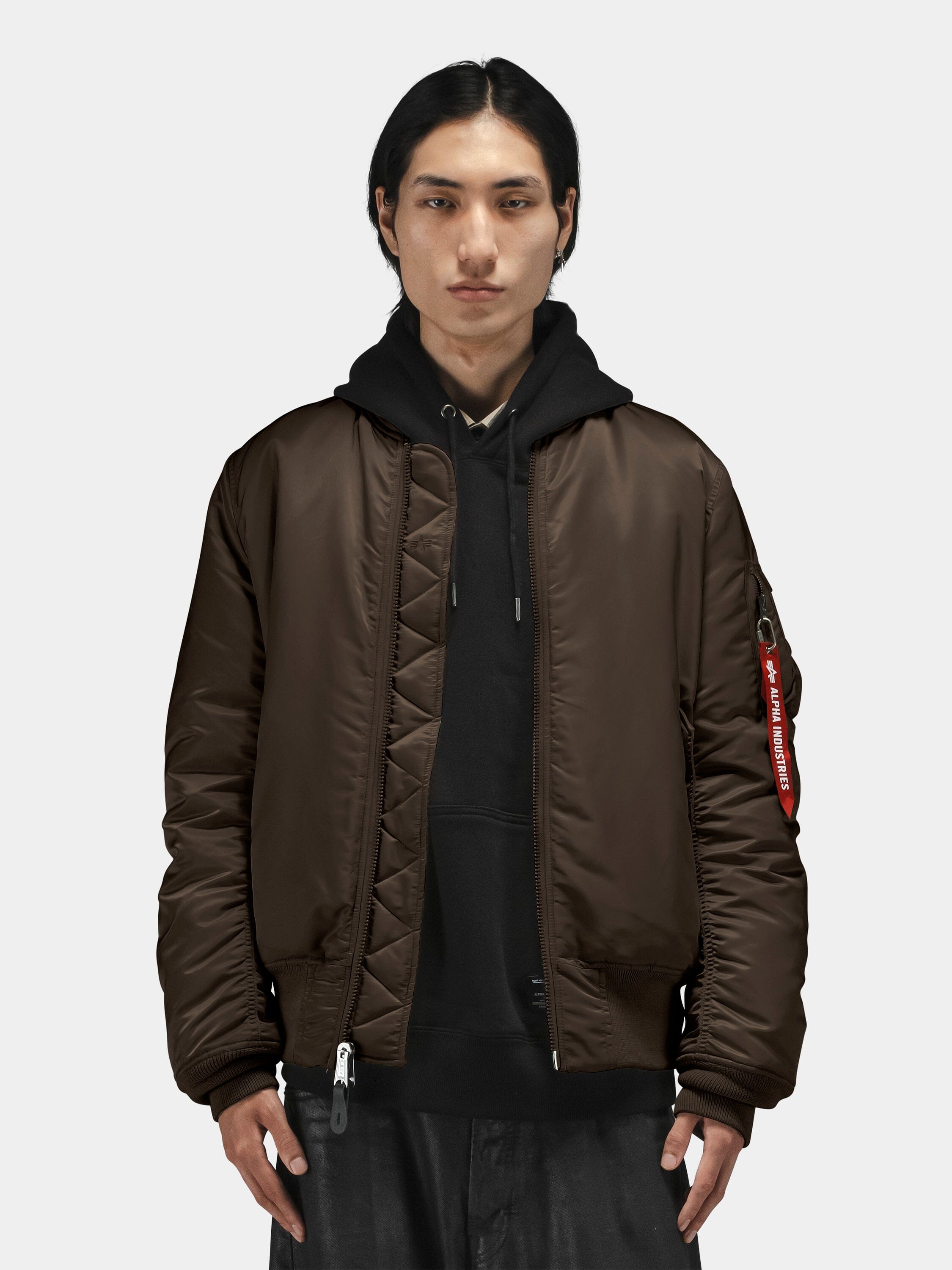 Alpha Industries MA-1 Bomber Jacket in dark color over a black hoodie; features zip closure and ribbed cuffs and hem.