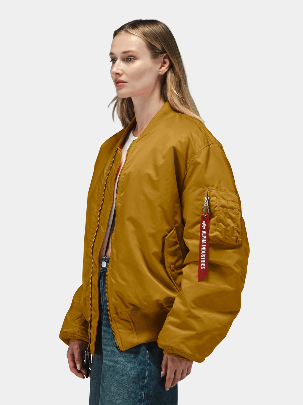 Mustard yellow Alpha Industries MA-1 Bomber Jacket with red Remove Before Flight tag on sleeve, blue jeans.