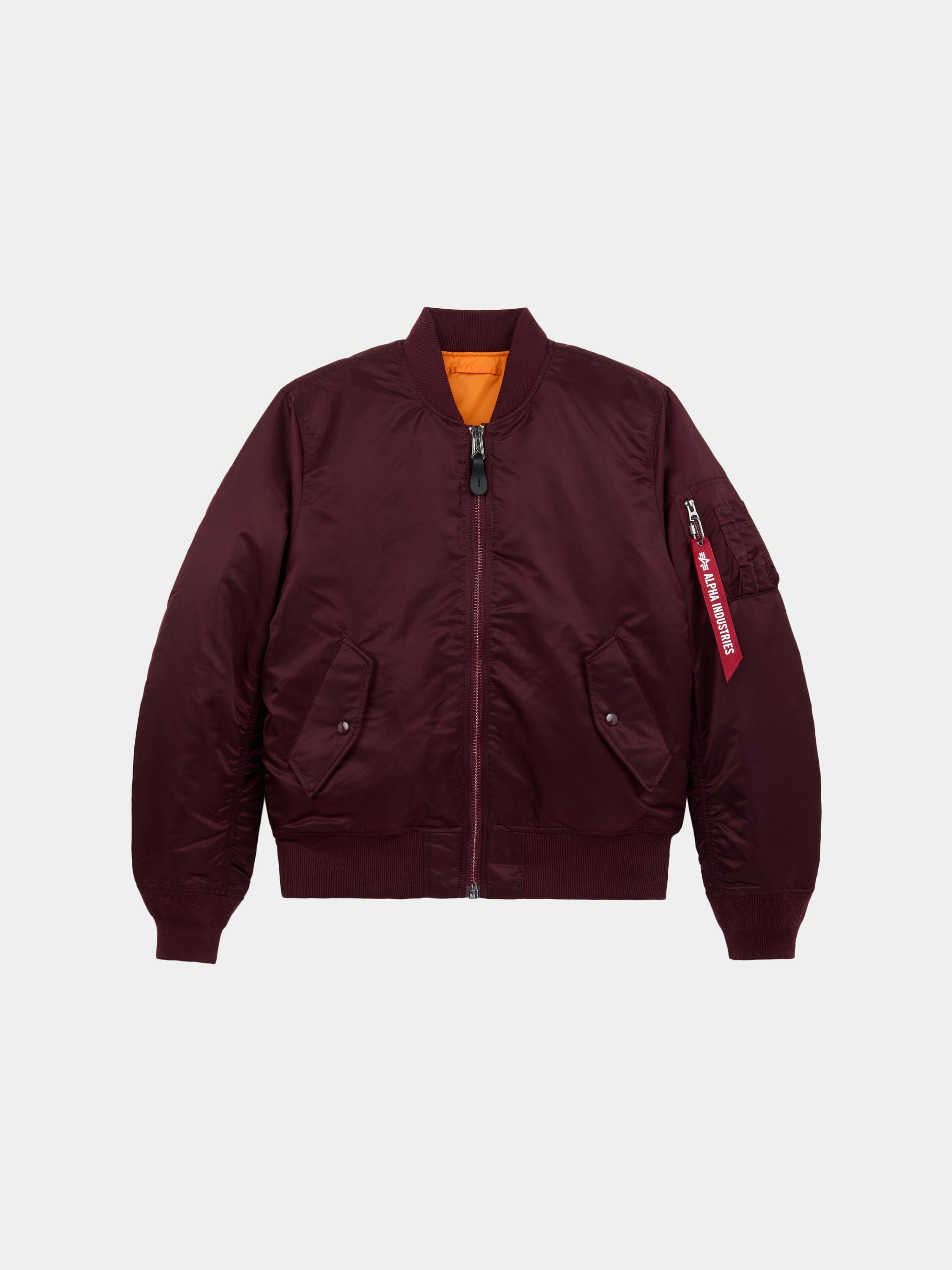 Front flat-lay view of cedar red Alpha Industries MA-1 Bomber Jacket Slim Fit showing ribbed collar, sleeve pocket with red tag, and orange lining at collar.