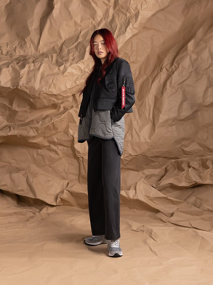 An person dressed in a layered ensemble that includes the Women's 3-In-1 MA-1 Quilted Liner in black, a cropped outer jacket by Alpha Industries.