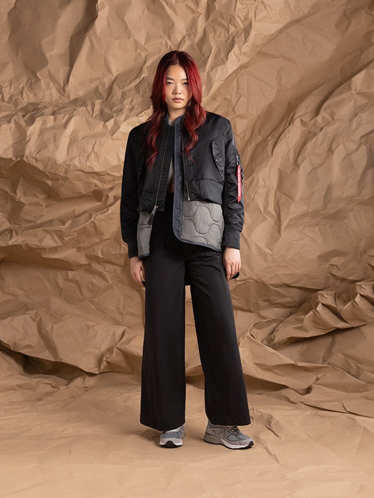 A person wearing the Women's 3-in-1 MA-1 Quilted Liner by Alpha Industries, styled with a cropped outer jacket and wide-leg pants.