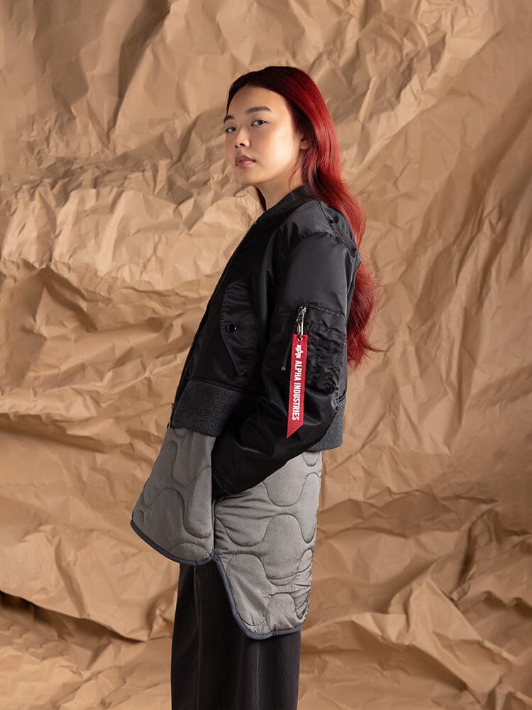 A person dressed in the Women's 3-In-1 MA-1 Quilted Liner by Alpha Industries, featuring a black and gray design with an onion quilted liner.