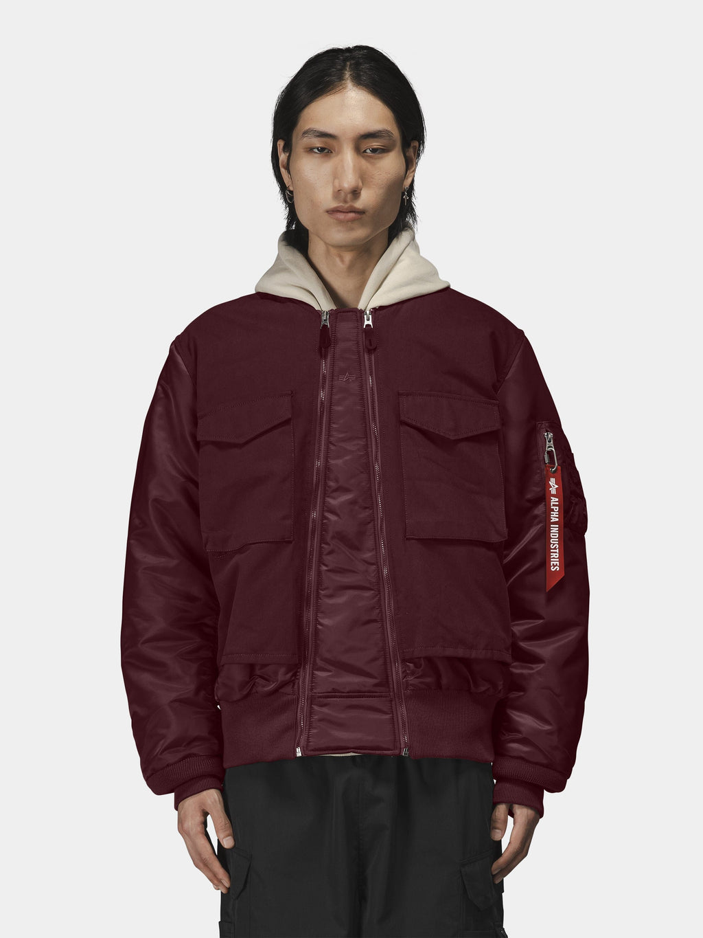Alpha Industries MA-1 Mixed Cotton Flight Jacket in burgundy with front pockets, beige hooded sweatshirt, and black pants.