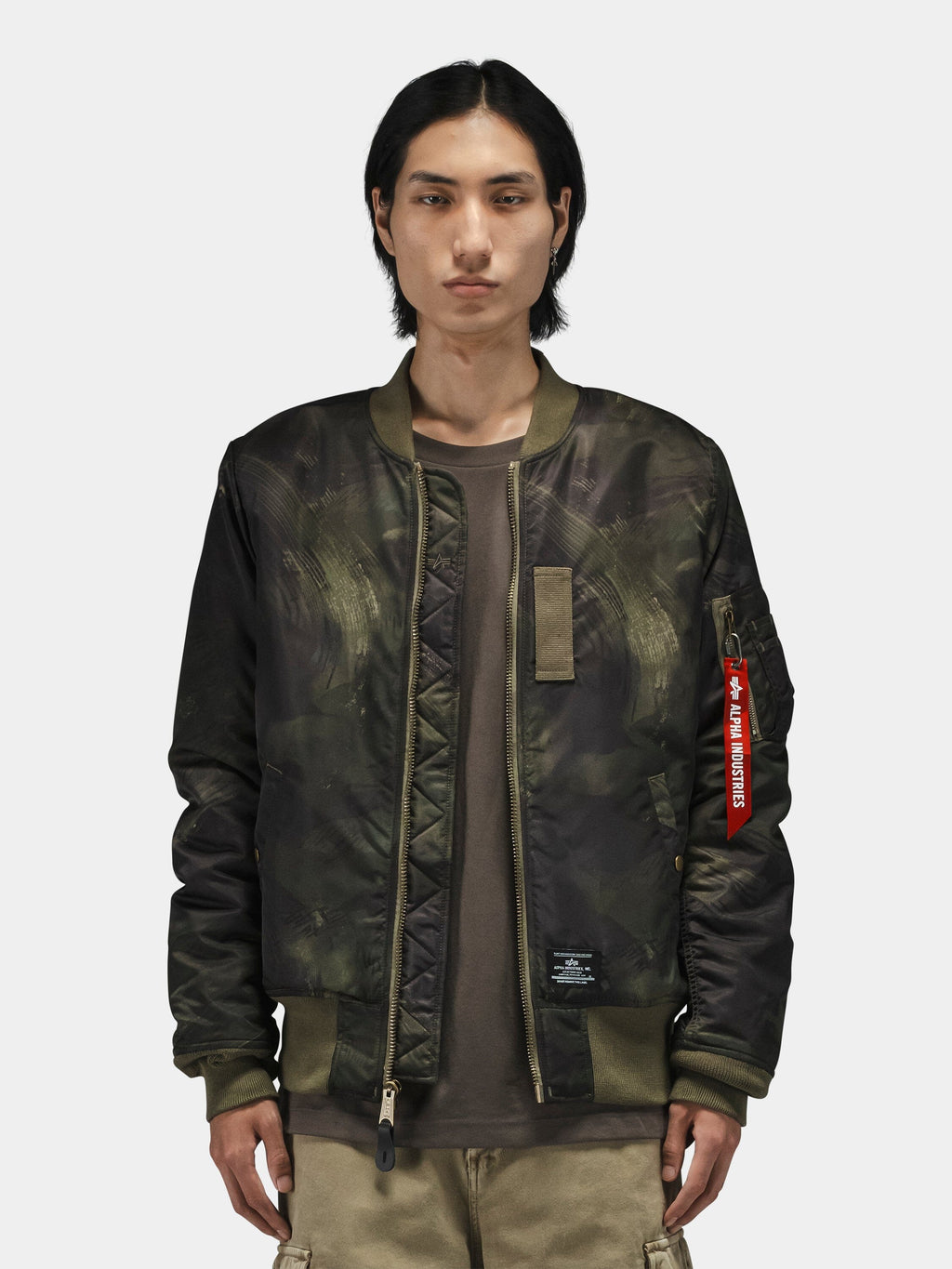 Alpha Industries MA-1 Mod Bomber Jacket in dark green camo with red Remove Before Flight tag and utility pocket.
