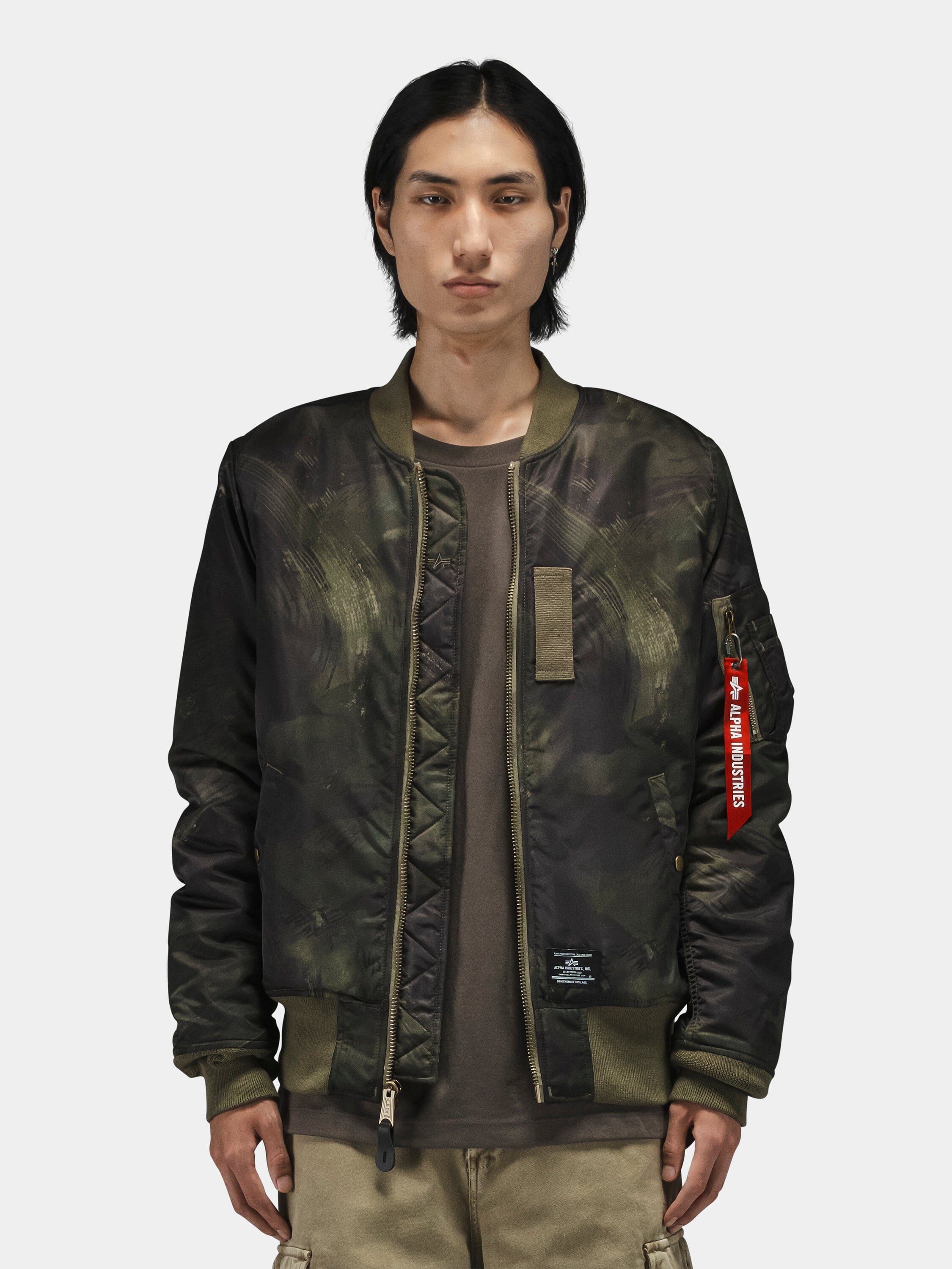 Alpha Industries MA-1 Mod Bomber Jacket in dark green camo with red Remove Before Flight tag and utility pocket.