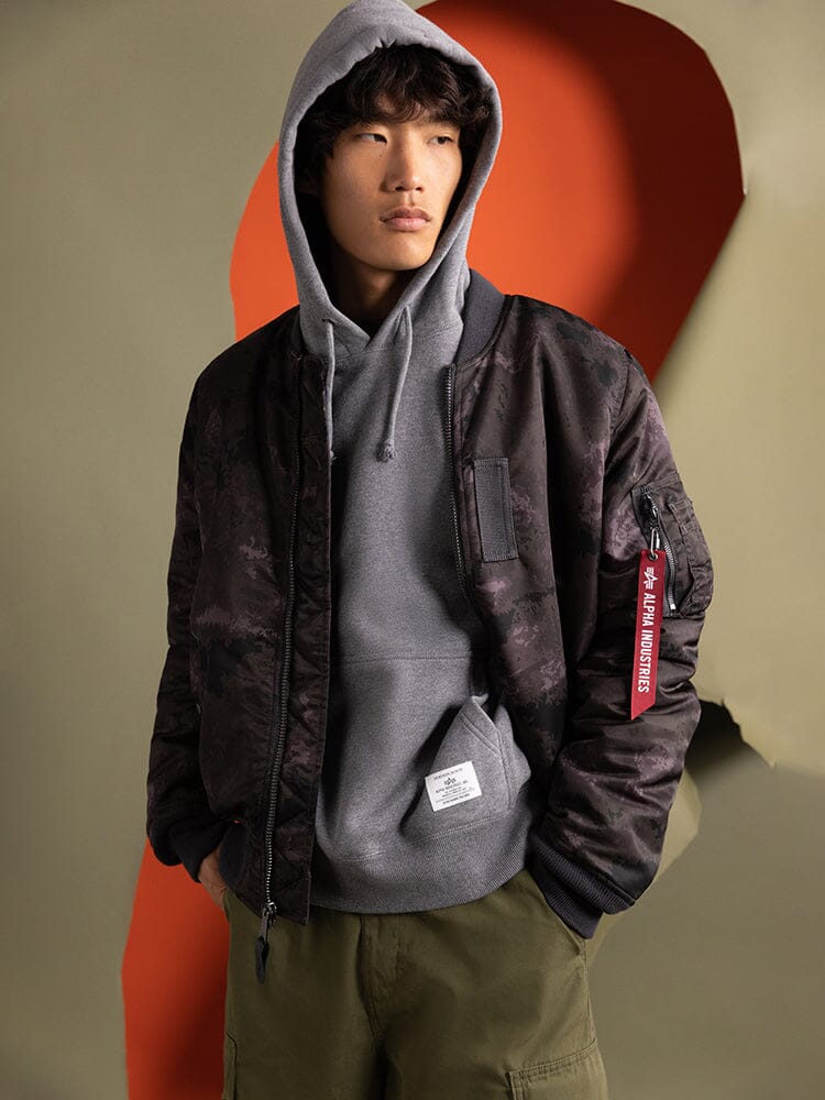 Alpha Industries MA-1 Mod Bomber Jacket with utility pocket, gray hoodie underneath, olive cargo pants.