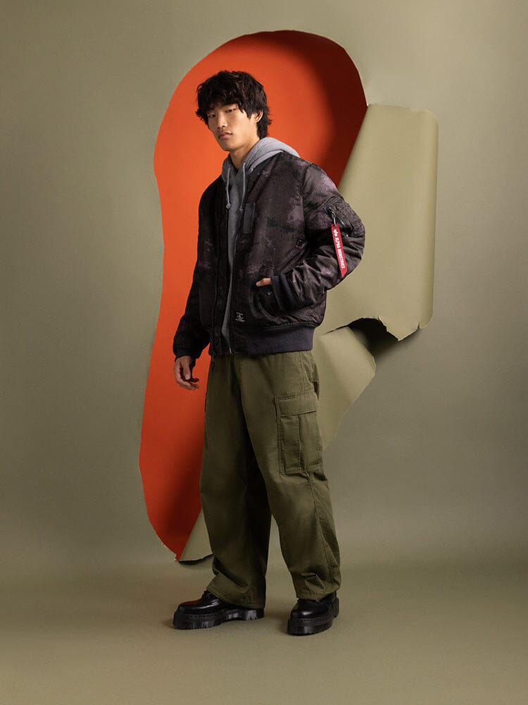Alpha Industries MA-1 Mod Bomber Jacket in olive green, gray hoodie, olive cargo pants with utility pockets, black platform shoes.