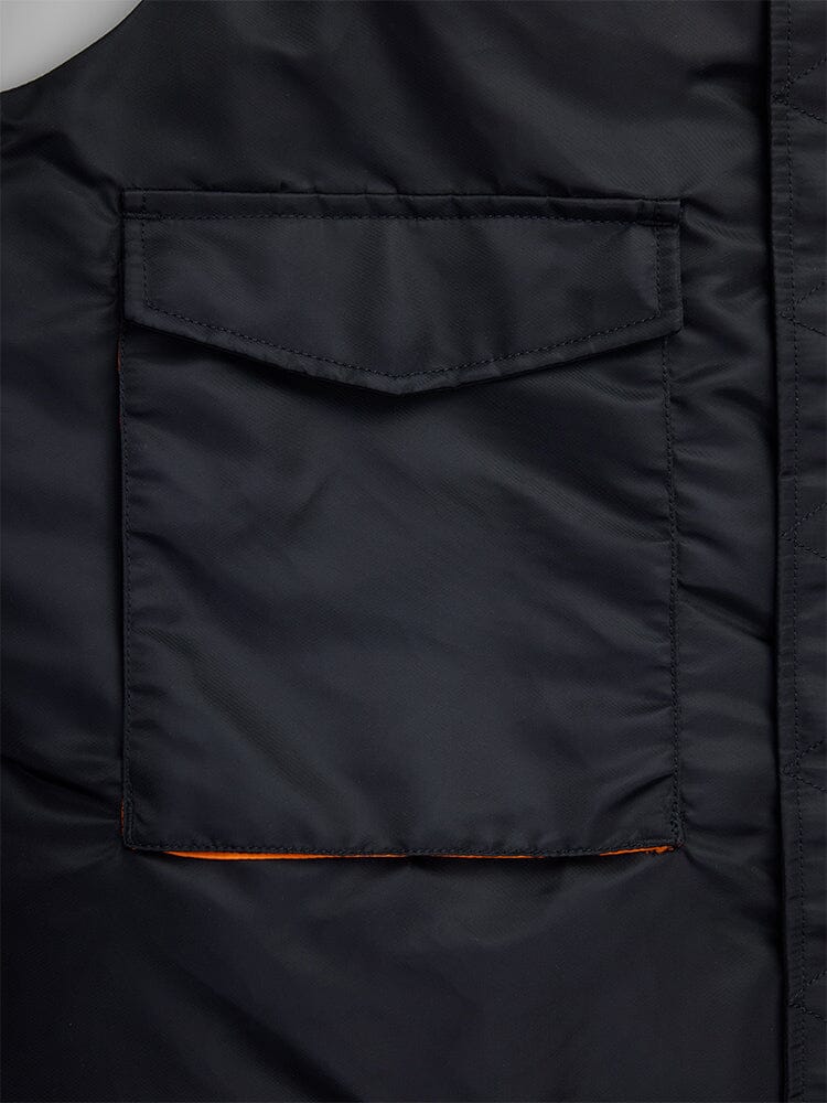 Close-Up of a black fabric pocket on the MA-1 Mod Vest by Alpha Industries, featuring a flap closure crafted from water-resistant material. The pocket interior is lined with vibrant orange rabric.
