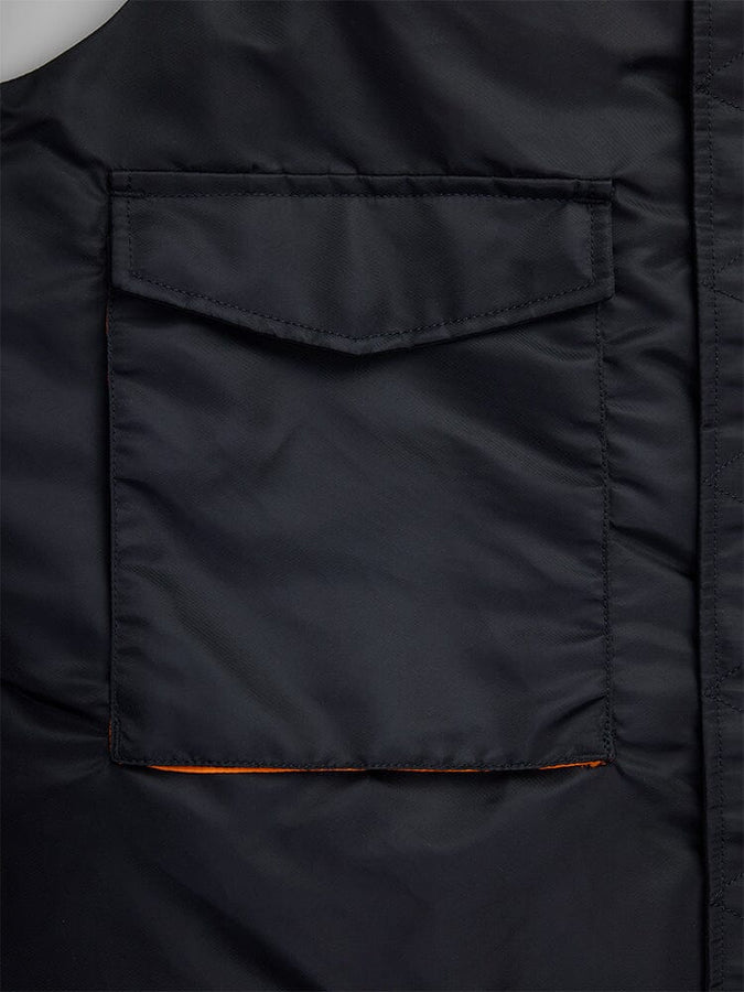 Close-Up of a black fabric pocket on the MA-1 Mod Vest by Alpha Industries, featuring a flap closure crafted from water-resistant material. The pocket interior is lined with vibrant orange rabric.