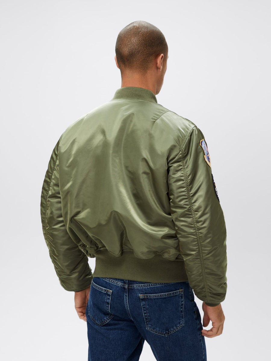 Alpha Industries MA-1 Squadron Bomber Jacket in olive green with squadron patches and blue jeans.