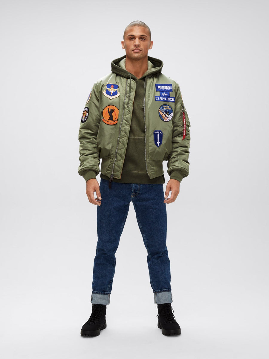 Alpha Industries MA-1 Squadron Bomber Jacket with squadron patches, olive hoodie, blue cuffed jeans, and black boots.
