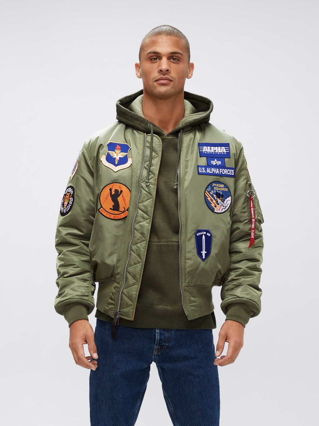 Alpha Industries MA-1 Squadron Bomber Jacket with squadron patches, layered over a green hoodie and blue jeans.
