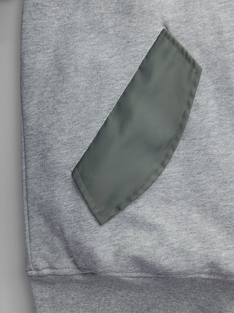 A close-up of MA-1 Zip Up Hoodie in gray by Alpha Industries, showcasing a green pocket detail sewn onto it.