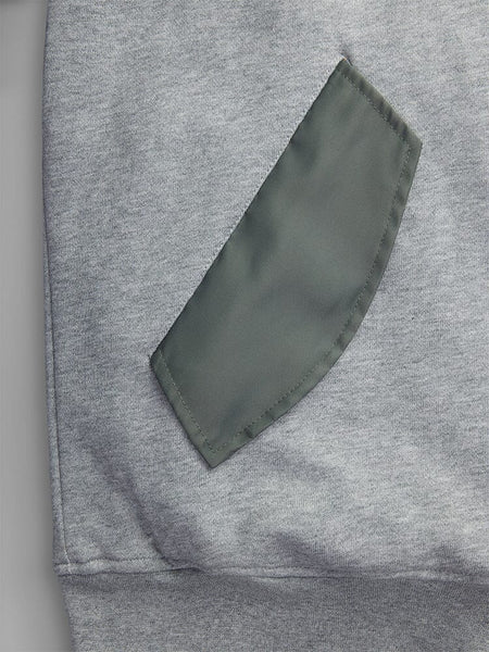 A close-up of MA-1 Zip Up Hoodie in gray by Alpha Industries, showcasing a green pocket detail sewn onto it.