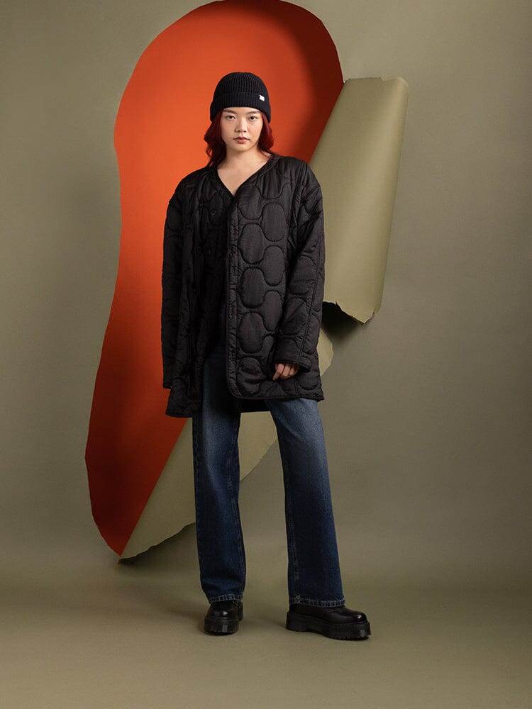 A person wearing the Women's Mixed Media Quilted Long Liner jacket in black by Alpha Industries.