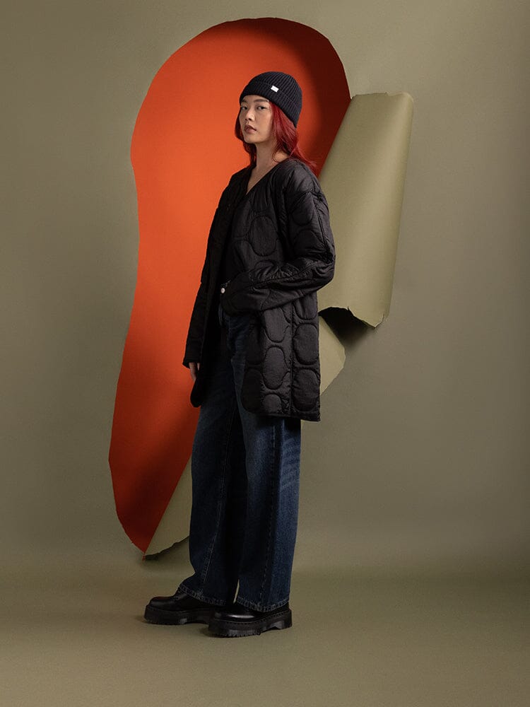 Side-view of a person wearing the Women's Mixed Media Quilted Long Liner in black by Alpha Industries.