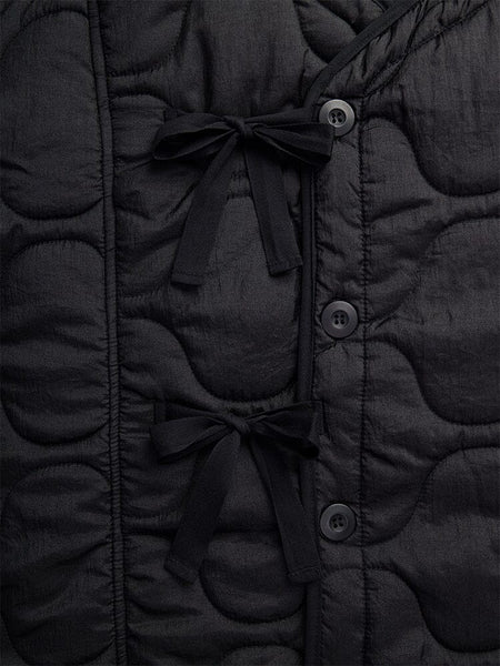 Close-up of the Women's Mixed Media Quilted Long Liner by Alpha Industries, showcasing its black quilted fabric adorned with two black bow ties and three vertically stitched black buttons in an onion quilting pattern.