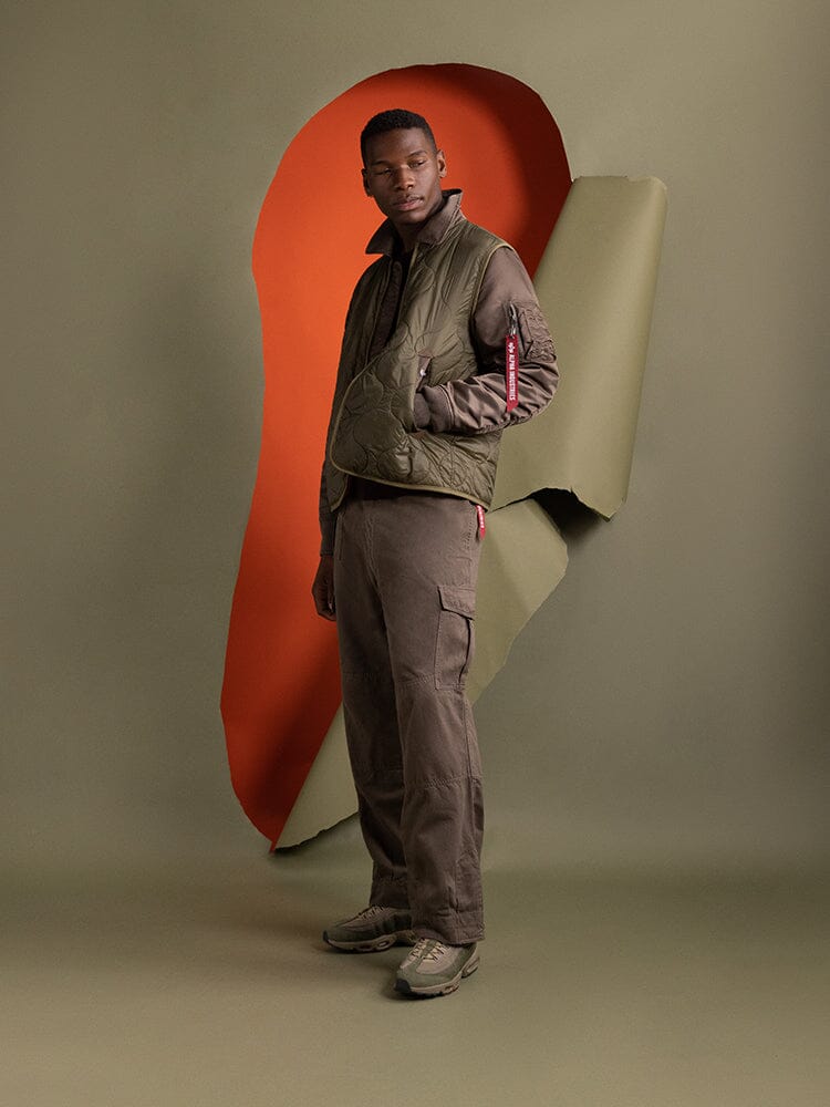 A person stands clad in an Alpha Industries Mixed Media Quilted Utility Jacket in coyote brown, with brown cargo pants.