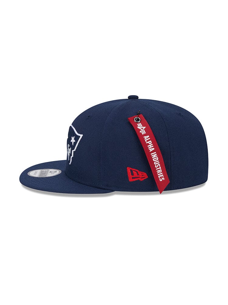 Navy blue New England Patriots x Alpha x New Era 950 Cap showcasing a logo on the front, with a red Alpha Industries tag and red New Era embroidery on the side.