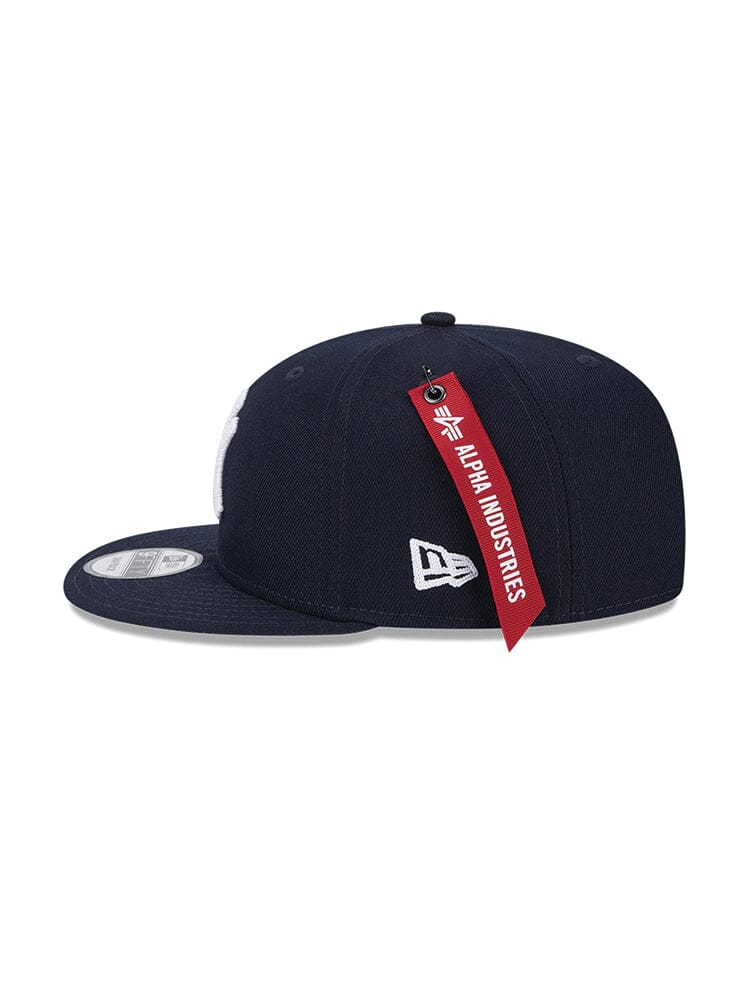 A navy blue New York Yankees x Alpha Industries x New Era 950 cap, boasting a flat bill, features a white embroidered team logo on the side and is accented with a red Alpha Industries tag attached to the back.