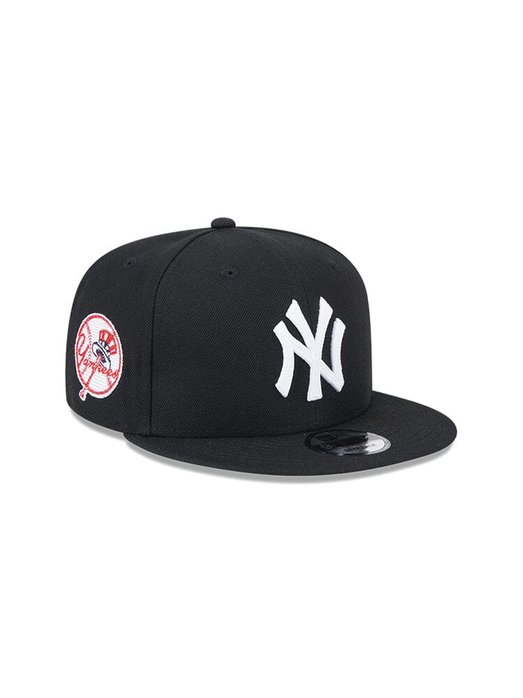 The New York Yankees x Alpha x New Era 950 Cap (Black) by Alpha Industries features a white NY team logo on the front and a circular red and white patch on the side.