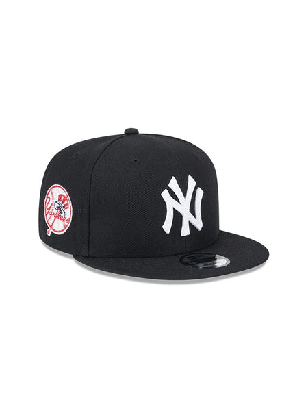The New York Yankees x Alpha x New Era 950 Cap (Black) by Alpha Industries features a white NY team logo on the front and a circular red and white patch on the side.