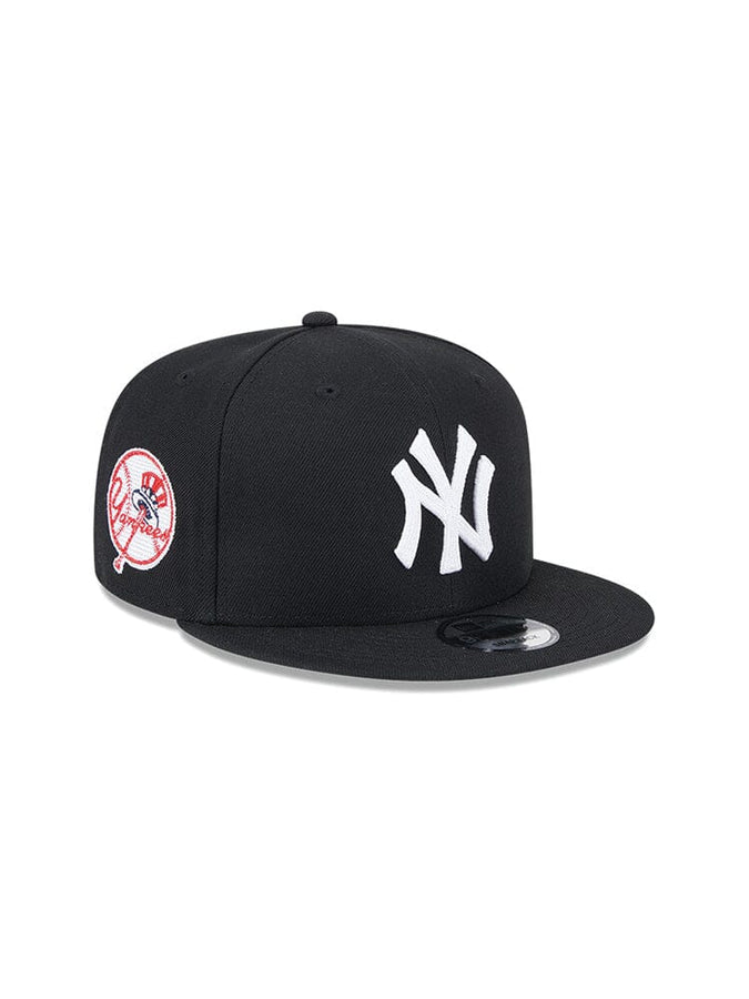 The New York Yankees x Alpha x New Era 950 Cap (Black) by Alpha Industries features a white NY team logo on the front and a circular red and white patch on the side.