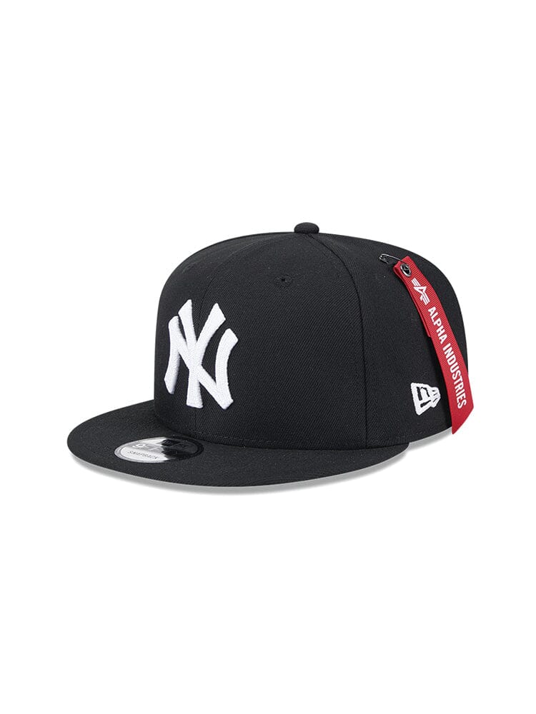 Introducing the New York Yankees x Alpha x New Era 950 Cap in black, designed by Alpha Industries. This snapback cap features a flat brim with a white New York Yankees team logo on the front and is accented with a red Alpha Industries tag on the side.