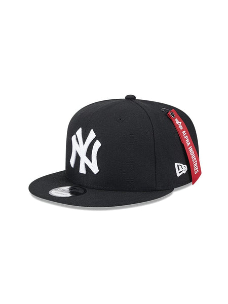 Introducing the New York Yankees x Alpha x New Era 950 Cap in black, designed by Alpha Industries. This snapback cap features a flat brim with a white New York Yankees team logo on the front and is accented with a red Alpha Industries tag on the side.