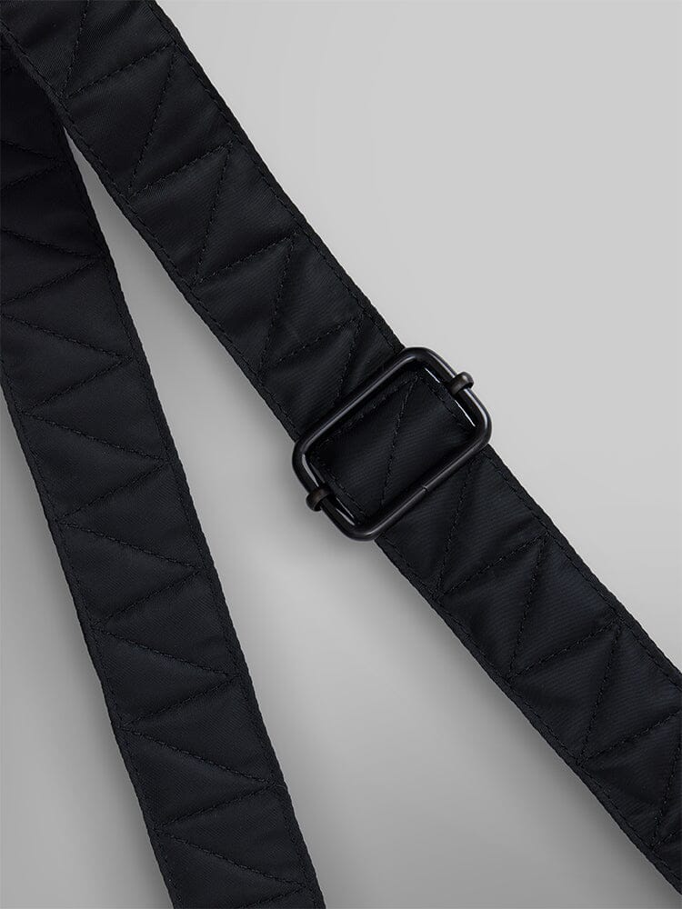 The Nylon Messenger Bag by Alpha Industries features a durable black quilted nylon strap with a zigzag pattern and a rectangular black buckle, enhanced by an adjustable shoulder strap.