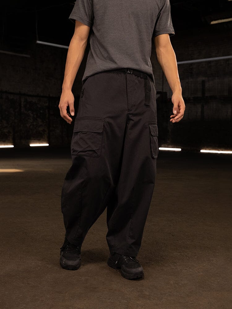 An individual dressed in Alpha Industries' Oversized Tactical Pant, featuring black wide cargo pockets and an elastic waistband, is seen standing.