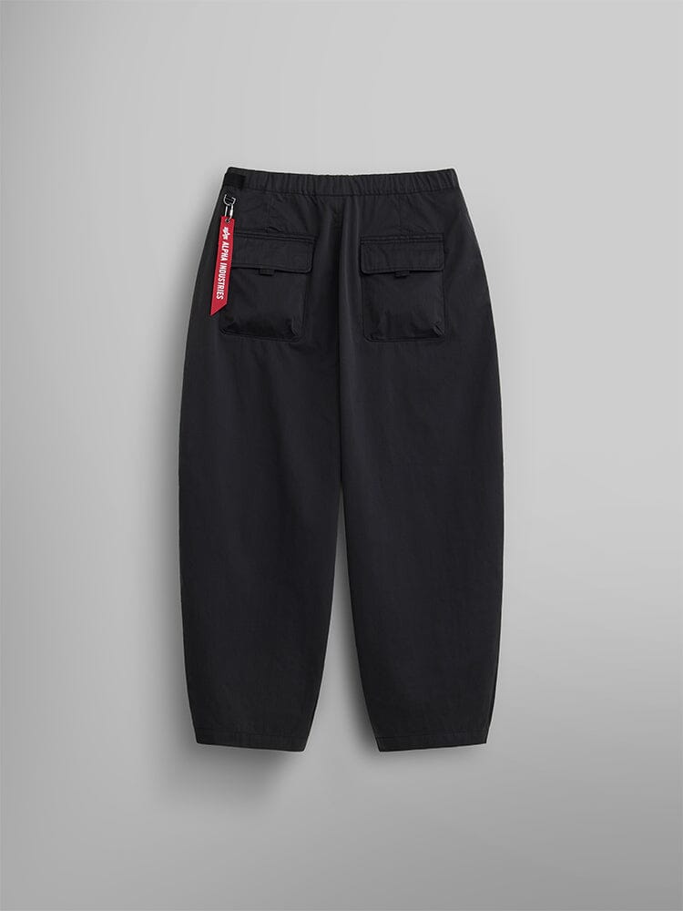 The Oversized Tactical Pant by Alpha Industries combines style and comfort with its black oversized design featuring an elastic waistband, two back pockets, and a distinctive red tag on the side.