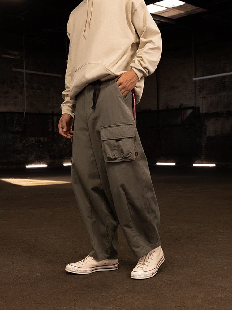 A person wearing an oversized beige hoodie, the Oversized Tactical Pant by Alpha Industries featuring cargo pockets in olive, and white sneakers.