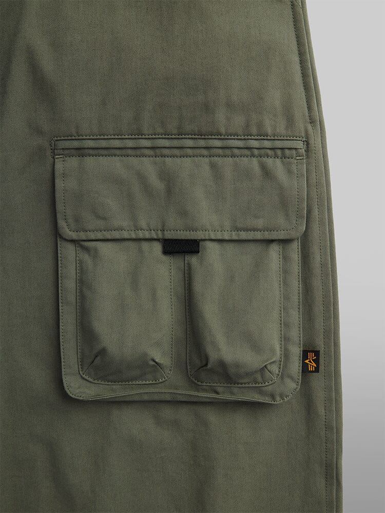 Close-up of an olive green fabric featuring a large cargo pocket and a small black and yellow tag on the right side, ideal for the Oversized Tactical Pant by Alpha Industries, perfect for adding style to oversized pants.