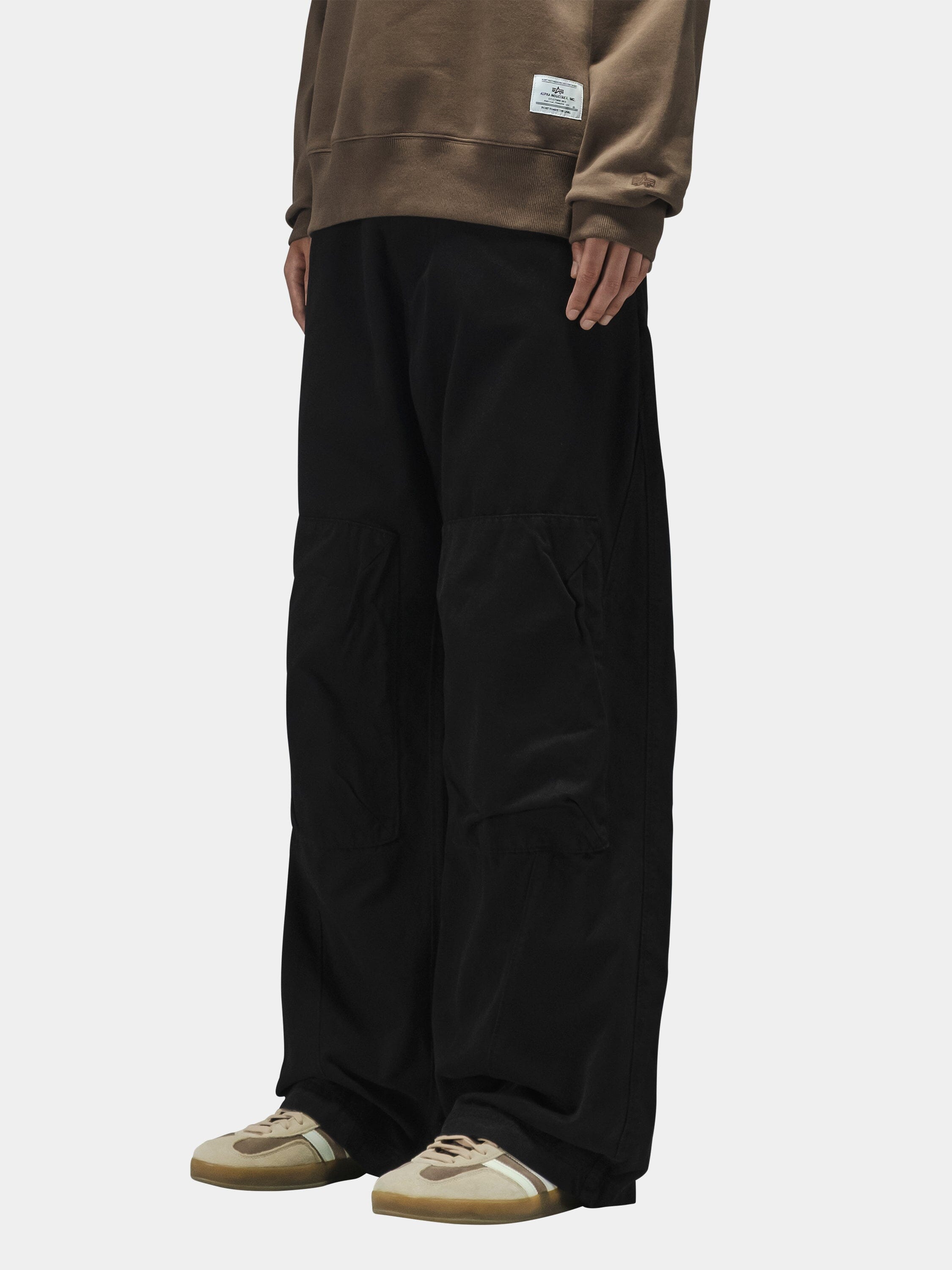 Alpha Industries Oversized Washed Pant, black cargo style with large knee patches. Brown sweatshirt and beige sneakers.