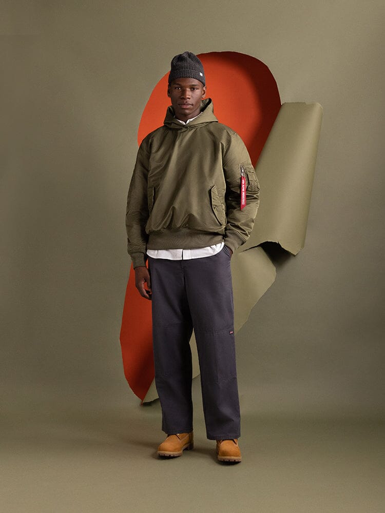 A person wearing the OG-107 Green Pull-Over MA-1 Jacket Hoodie by Alpha Industries.