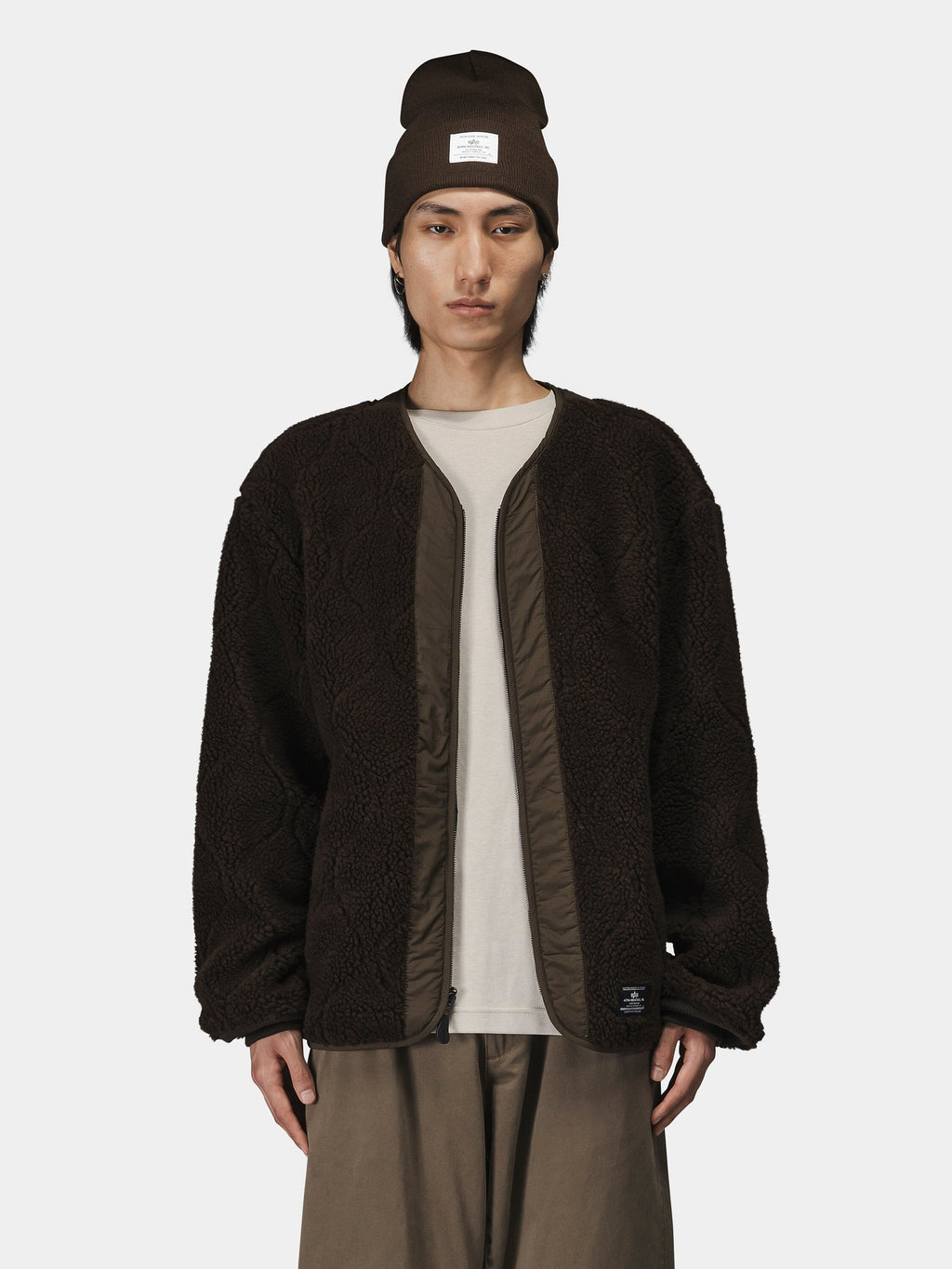 Alpha Industries Reversible M-65 Quilted Liner, brown beanie, beige shirt, brown pants.