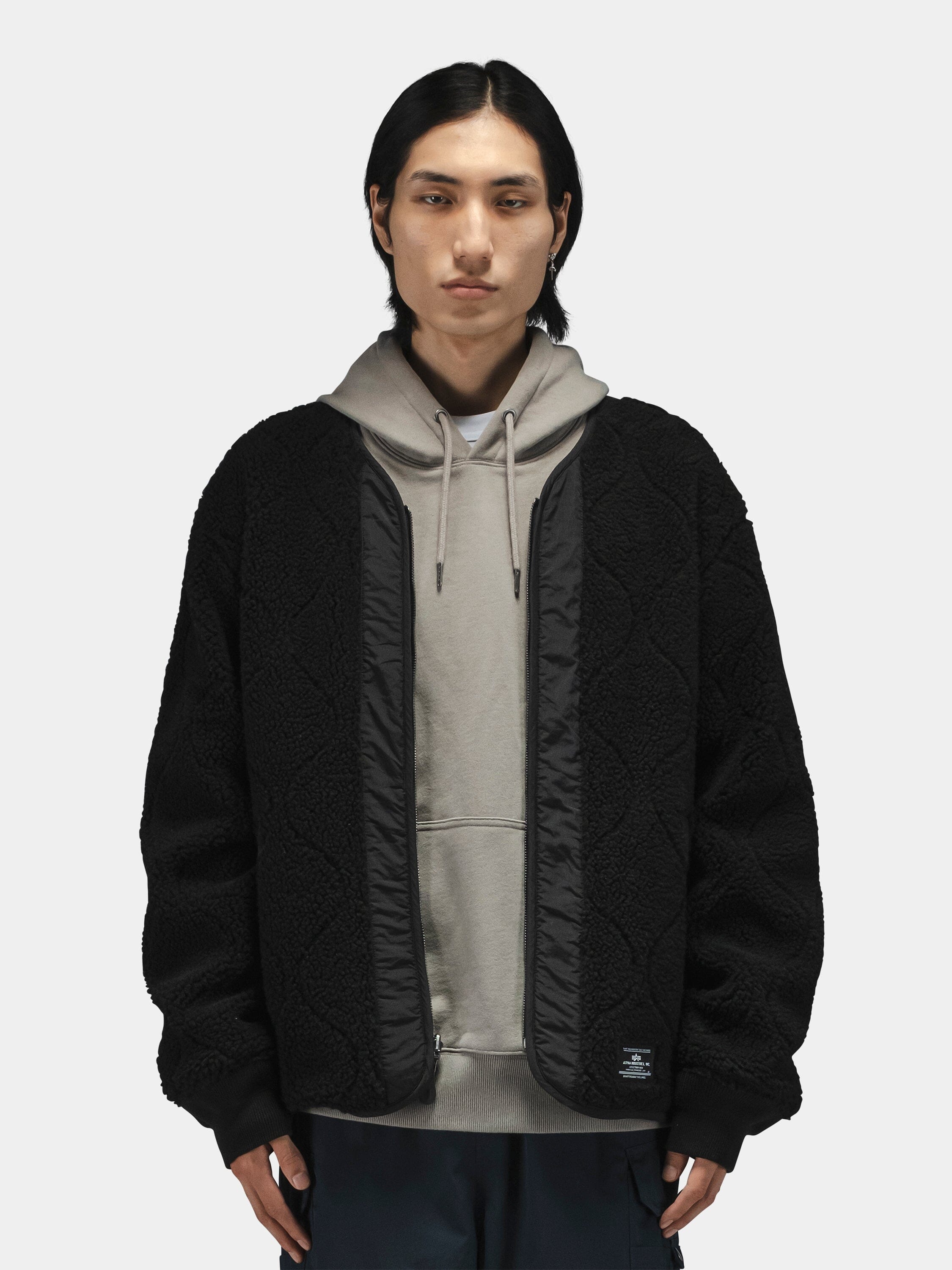 Alpha Industries Reversible M-65 Quilted Liner, black camo with dark trim, layered over a grey hoodie.