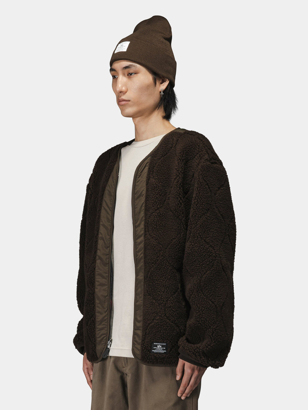 Alpha Industries Reversible M-65 Quilted Liner jacket in textured pattern, brown beanie, white t-shirt, brown pants.