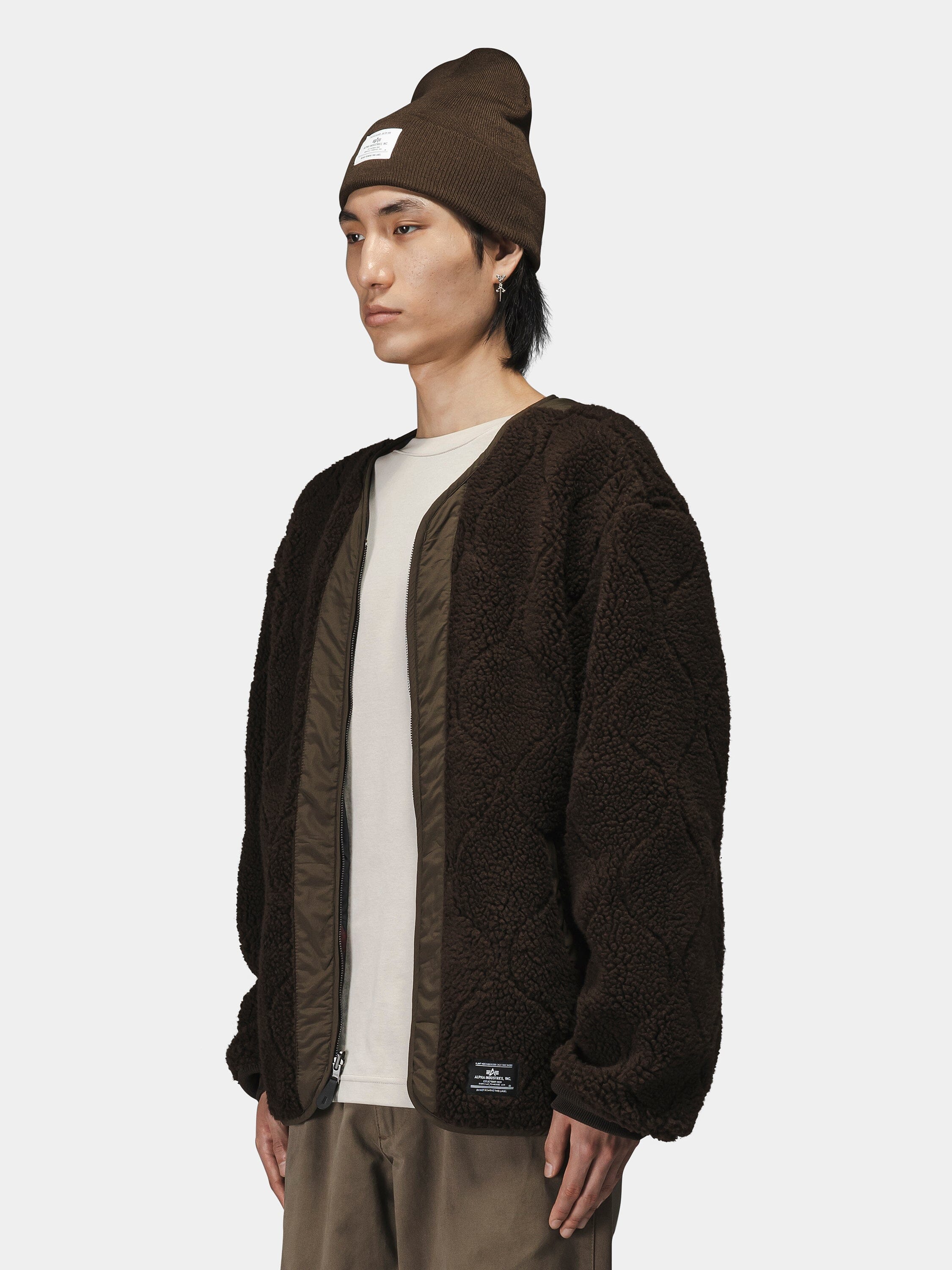 Alpha Industries Reversible M-65 Quilted Liner jacket in textured pattern, brown beanie, white t-shirt, brown pants.