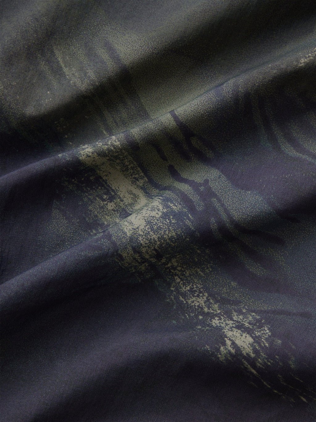 Alpha Industries Reversible M-65 Quilted Liner dark fabric with abstract camo pattern, visible folds, and quilted reversible texture.