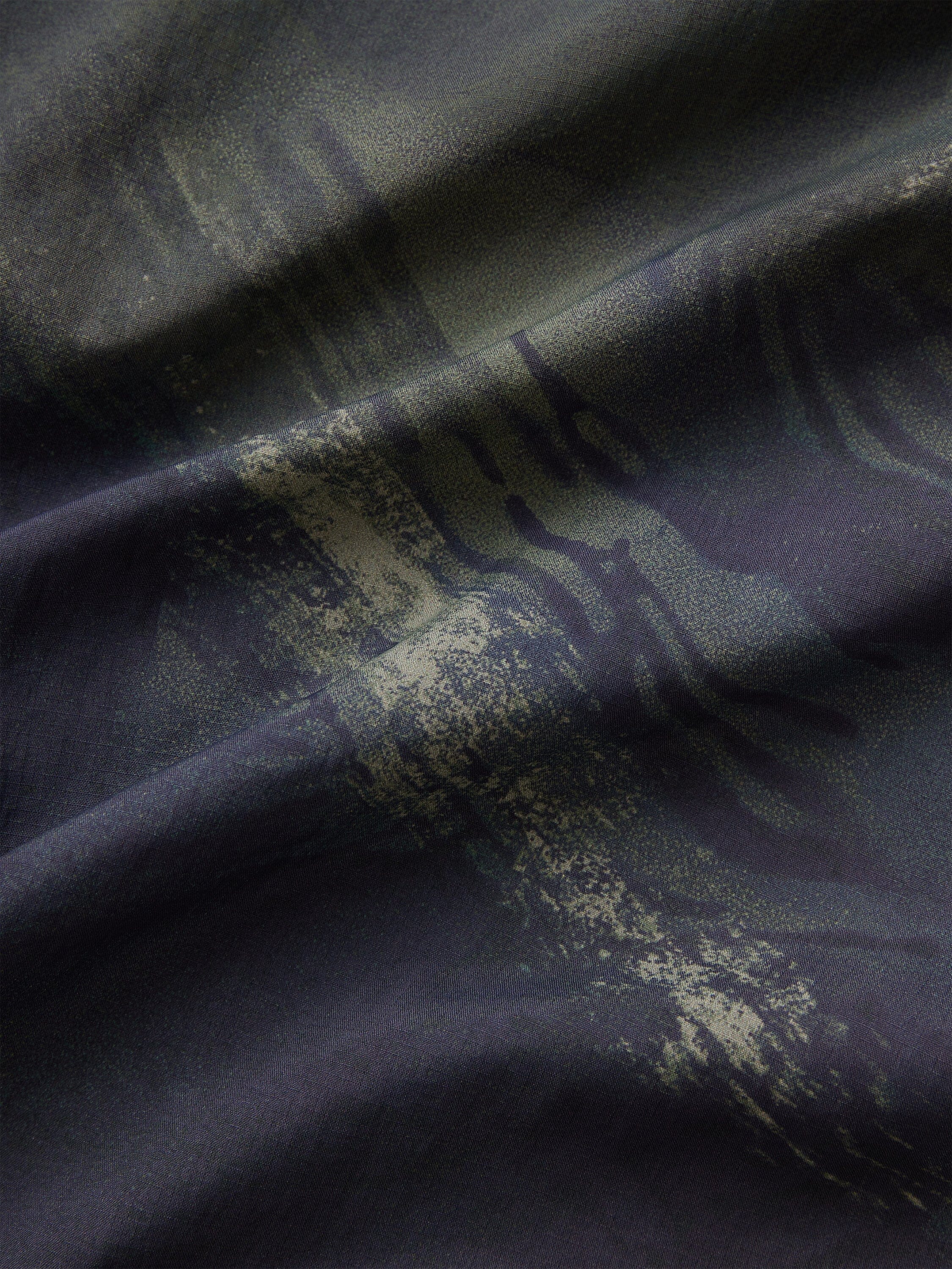 Alpha Industries Reversible M-65 Quilted Liner dark fabric with abstract camo pattern, visible folds, and quilted reversible texture.