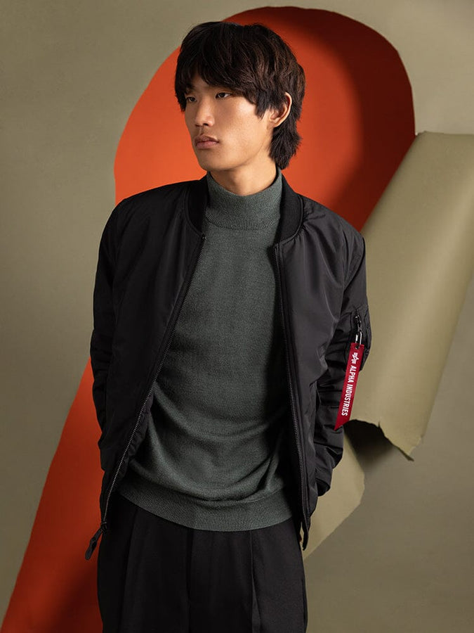 A person wearing the Reversible Onion Quilted MA-1 Bomber Jacket in black by Alpha Industries.