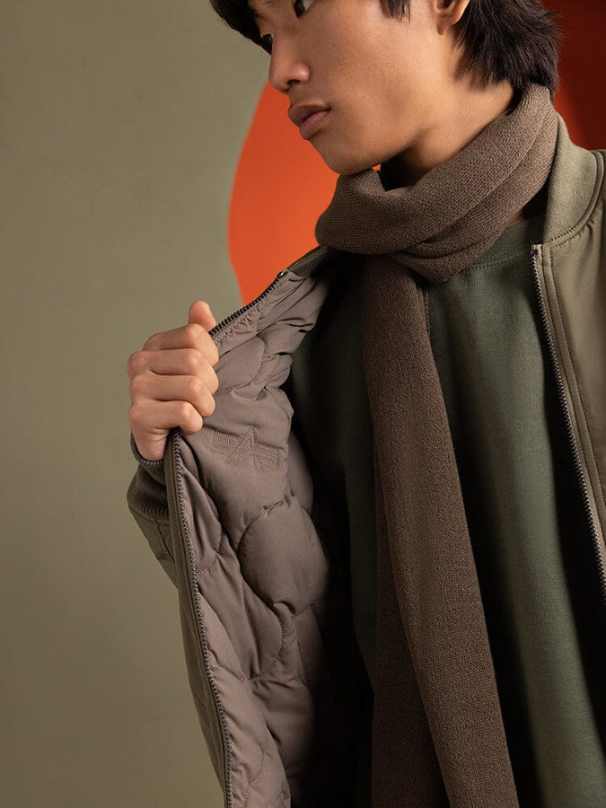 Close up view of a person wearing the Reversible Onion Quilted MA-1 Bomber Jacket in green by Alpha Industries. Person is holding open the jacket to show its lining.