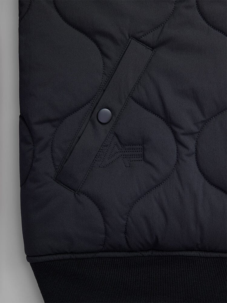Close-up of the pocket of the Reversible Onion Quilted MA-1 Bomber Jacket in black by Alpha Industries, featuring a buttoned pocket and textured quilted pattern, made from water-resistant nylon.