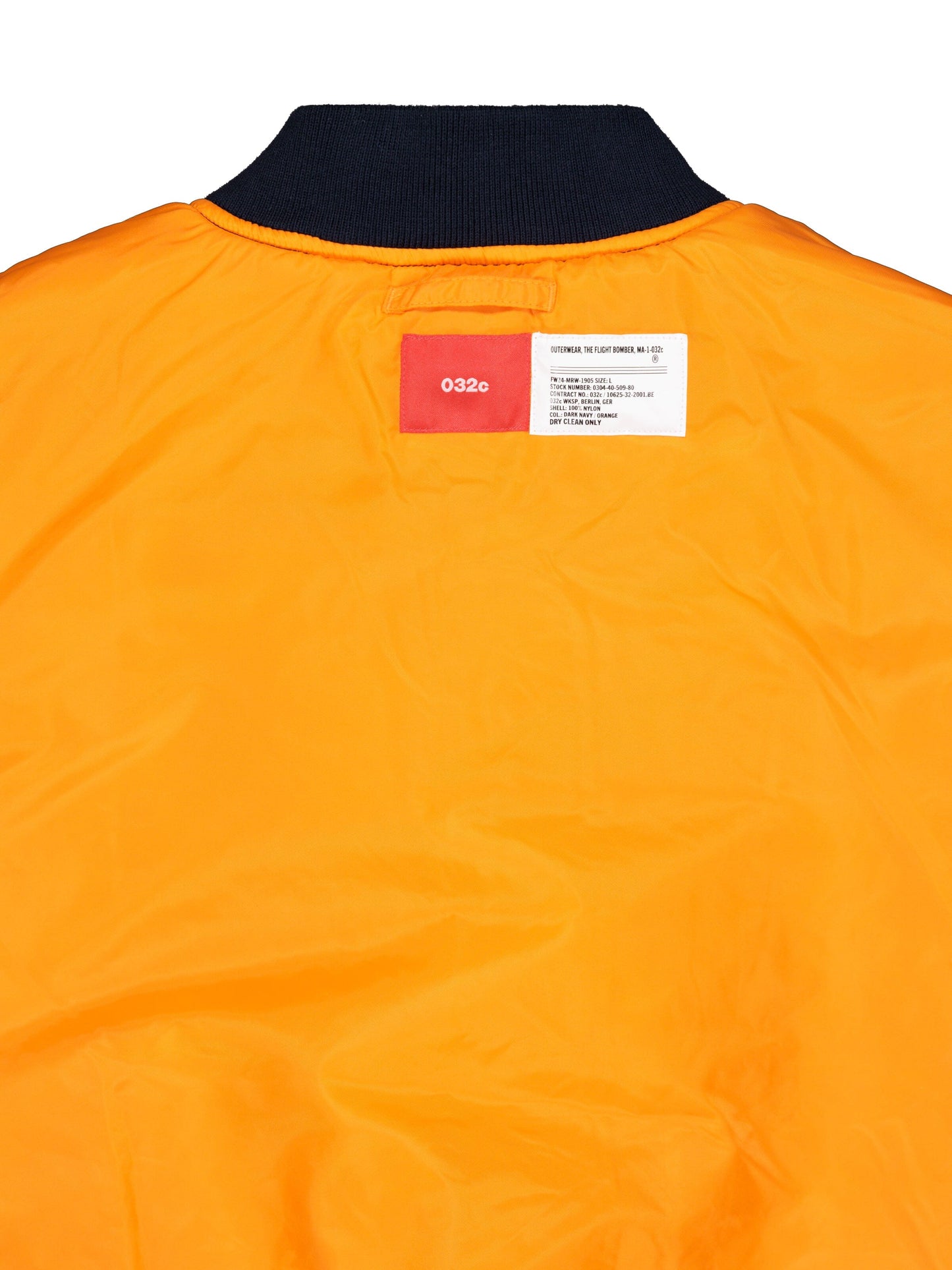 Alpha X 032c Flight Bomber by Alpha Industries, orange Flight Nylon fabric, black collar, two rectangular labels near neckline, MA-1 style.