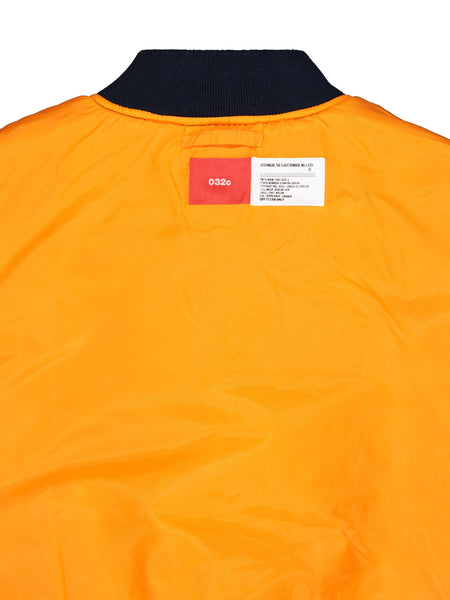Alpha X 032c Flight Bomber by Alpha Industries, orange Flight Nylon fabric, black collar, two rectangular labels near neckline, MA-1 style.