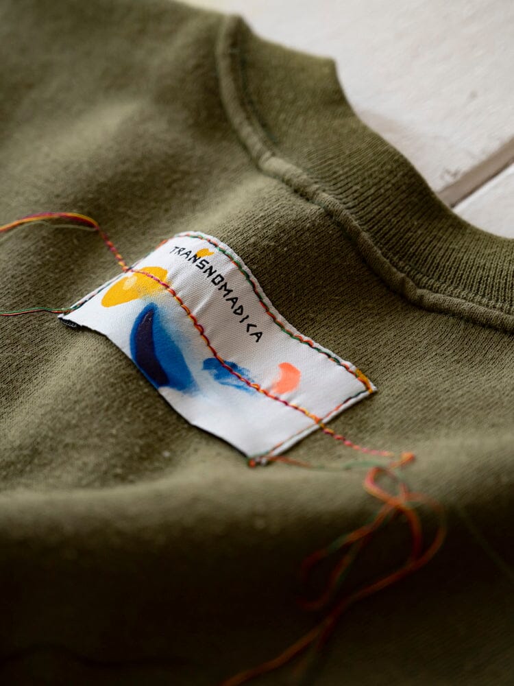 Transnomadica X Alpha Upcycled USMC Sweatshirt by Alpha Industries, green upcycled vintage sweatshirt with colorful, partially hand-stitched Transnomadica label and loose multicolored threads.