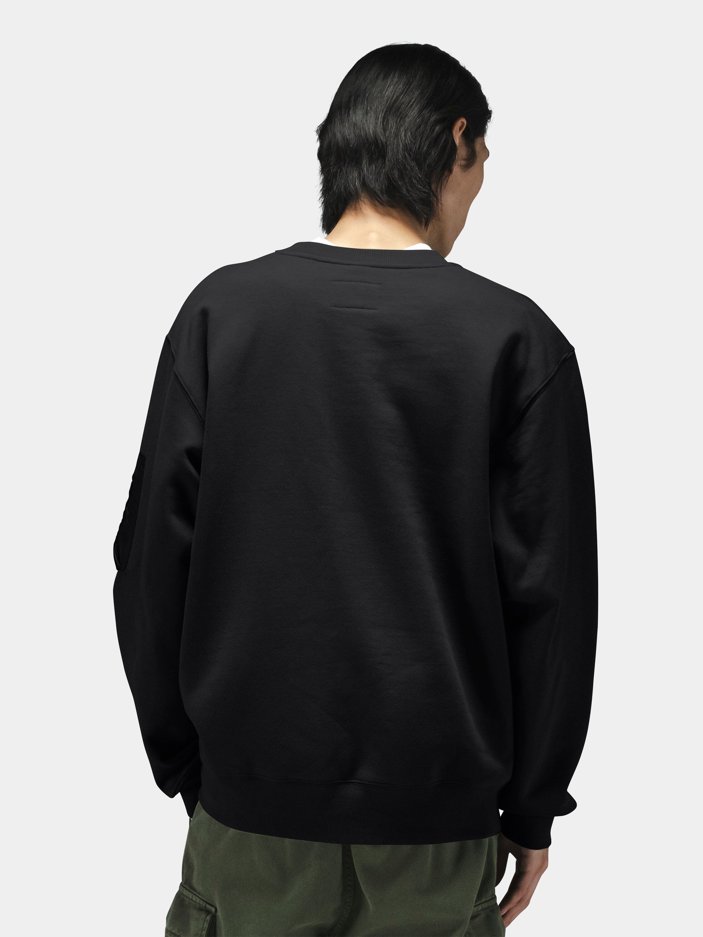 Alpha Industries Utility Pocket Crewneck in black, paired with olive green pants.