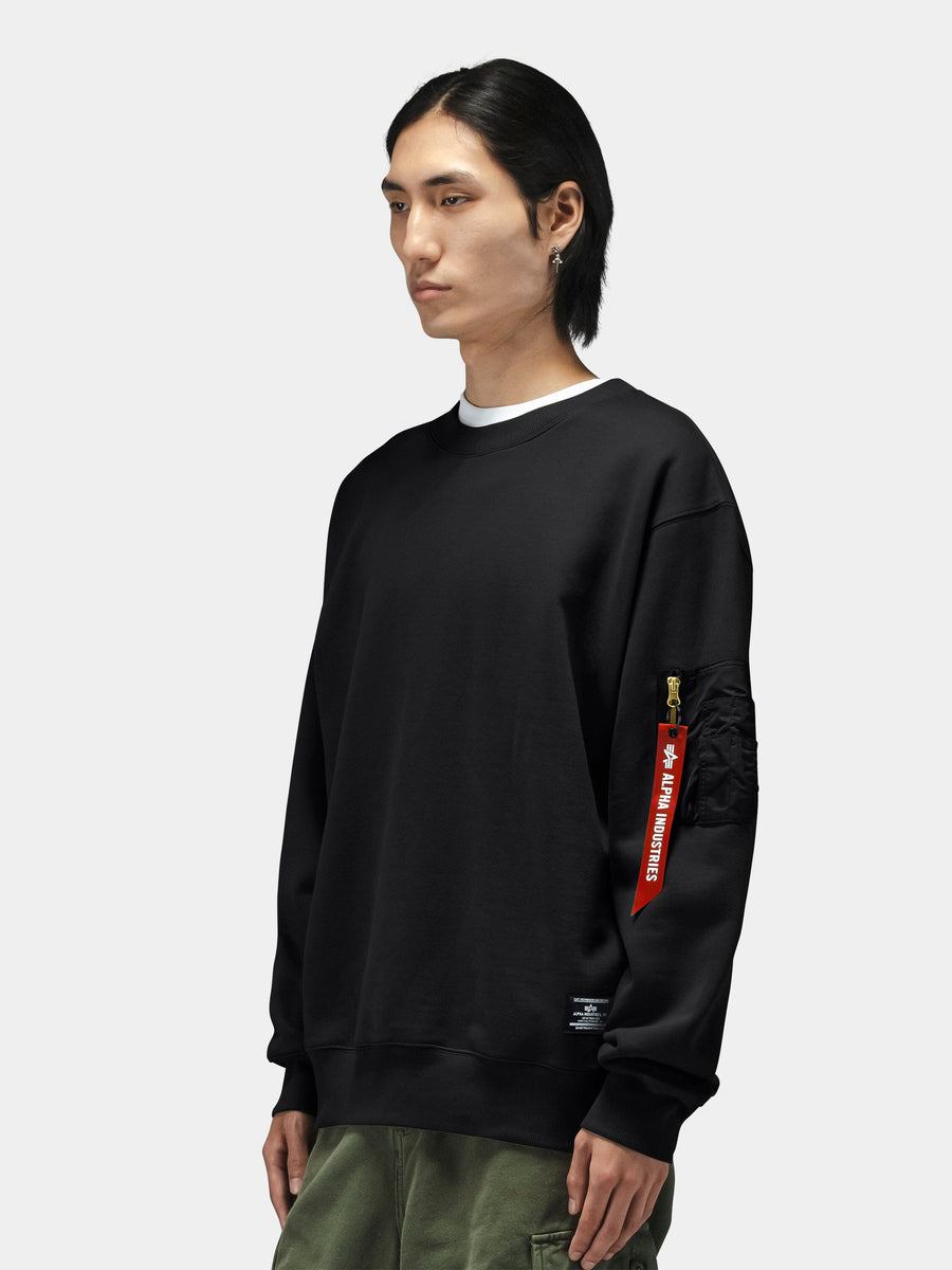 Alpha Industries Utility Pocket Crewneck with black MA-1 utility pocket and red tag, paired with olive green pants.